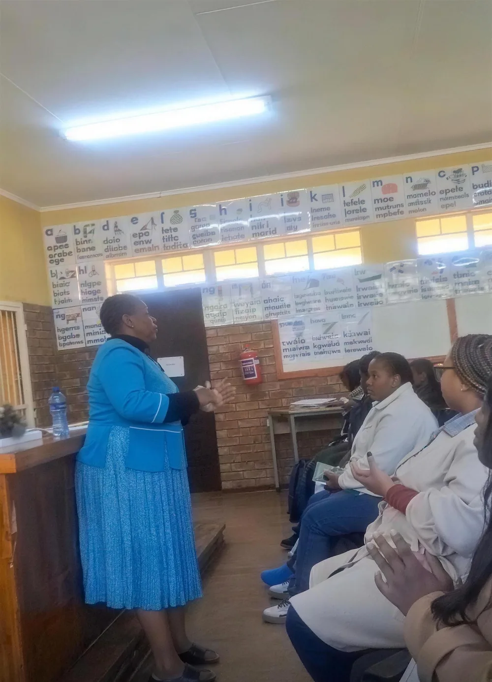 A Read Today SA facilitator addresses foundation phase educators seated in a classroom, with phonics charts covering the wall behind her