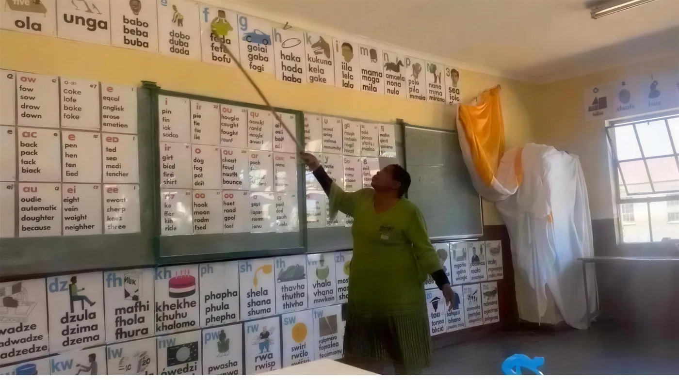 A Read Today SA trainer points to phonics charts covering the walls of a foundation phase classroom, showing the full Tshivenda and English poster set in place